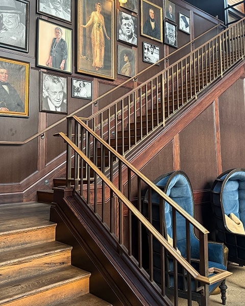 Eine edle Holztreppe mit Porträtwand und blauen Samtsesseln im historischen Oxford Exchange in Tampa.