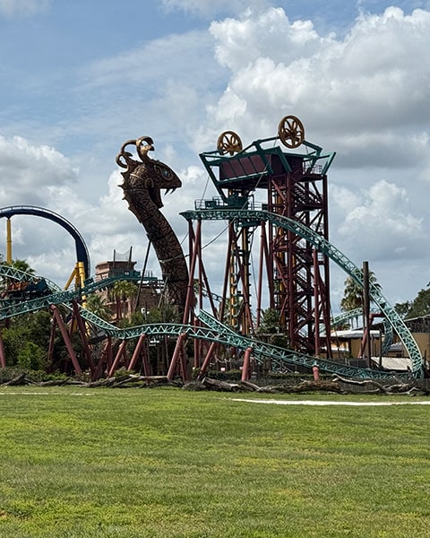 Die Achterbahn „Cobra’s Curse“ in Busch Gardens Tampa mit einer riesigen Schlangenstatue an den Schienen vor blauem Himmel.