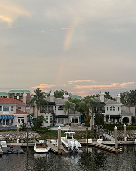 Ein Regenbogen steht über luxuriösen Uferhäusern und am Steg liegenden Booten in Tampa Bay bei Abenddämmerung.