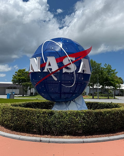 Das berühmte, kugelförmige blaue NASA-Logo inmitten eines runden Heckenbeets am Eingang des Kennedy Space Centers.