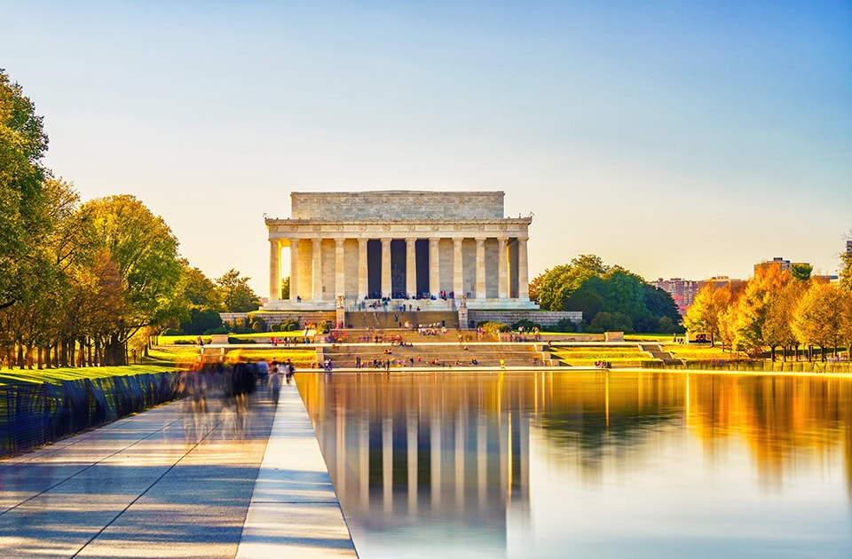 Das Lincoln Memorial in Washington, D.C. im warmen Licht der Abendsonne, dessen Säulenfassade sich perfekt im spiegelglatten Wasser des Reflecting Pools spiegelt.