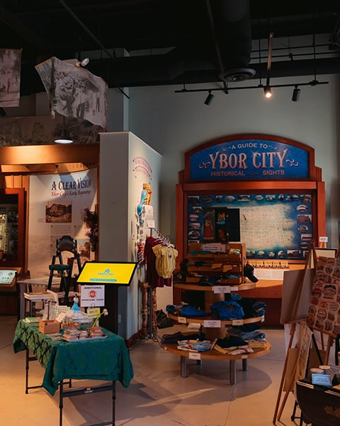 Ein Museums-Souvenirshop mit Infotafeln zu Ybor City, Verkaufsständern für Kleidung und einem Tisch mit Souvenirs.