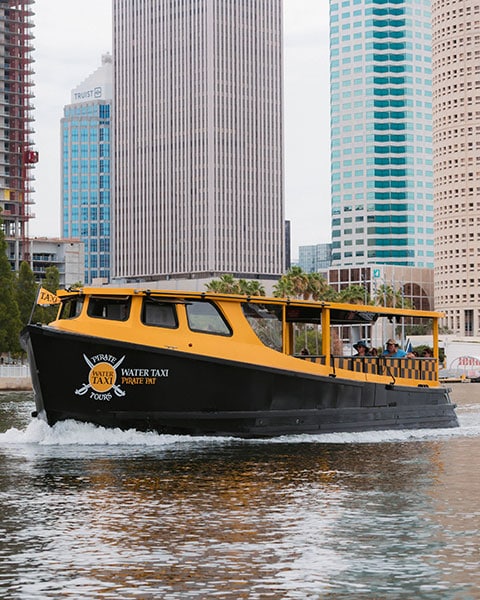 Ein gelb-schwarzes „Pirate Water Taxi“ fährt auf dem Wasser vor der Skyline von Downtown Tampa.
