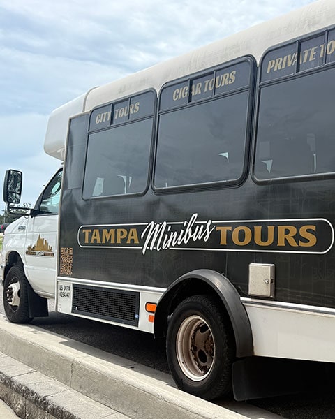 Ein weiß-schwarzer Minibus von „Tampa Minibus Tours“ steht am Straßenrand unter bewölktem Himmel.