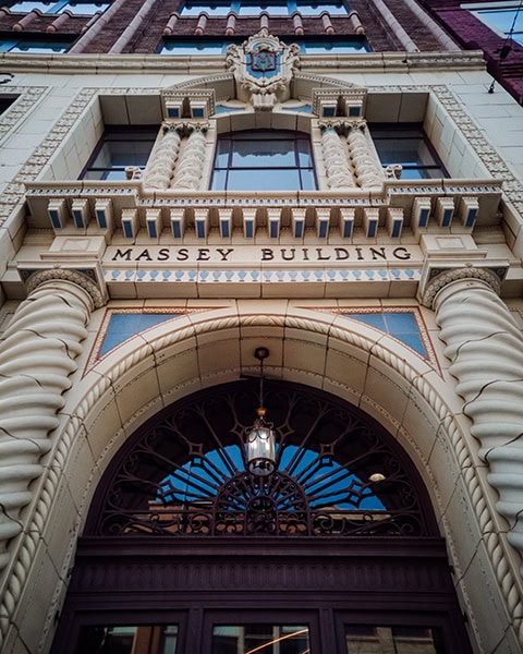 Ein prächtiges, historisches Portal aus hellem Naturstein zeigt den eingemeißelten Schriftzug „MASSEY BUILDING“ über einem großen Rundbogeneingang mit verzierten, gedrehten Säulen und einer hängenden Laterne.