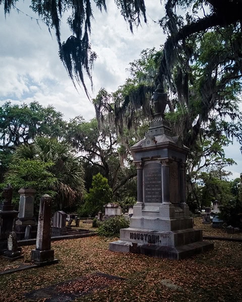 Ein monumentales, graues Steingrabmal mit der Aufschrift „HOUSTOUN“ steht inmitten historischer Grabsteine auf dem berühmten Bonaventure Cemetery in Savannah, Georgia, überspannt von alten Eichen mit dicht herabhängendem Spanischen Moos unter einem bewölkten Himmel.