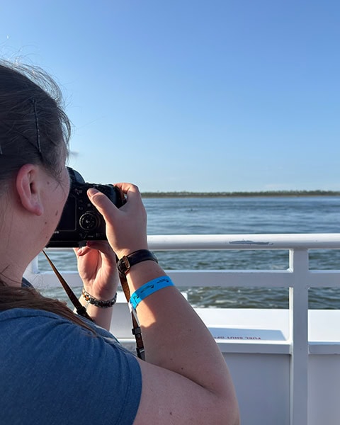 Eine Frau fotografiert von Bord eines Ausflugsboots der Cetacean Cruises aus mit einer Spiegelreflexkamera die weite Wasseroberfläche der Mobile Bay vor Orange Beach unter einem strahlend blauen Himmel.