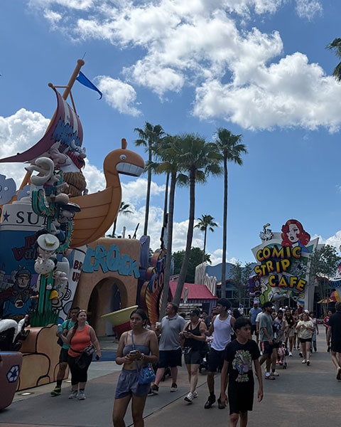 Menschen spazieren im Toon Lagoon Bereich der Universal Islands of Adventure an bunten Comic-Bauten und dem Comic Strip Cafe vorbei.