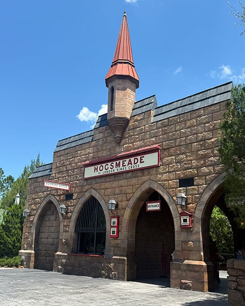 Das steinerne Bahnhofsgebäude der Hogsmeade Station mit spitzem Turm und dem Schild „Hogsmeade to London King's Cross“ in den Universal Islands of Adventure.