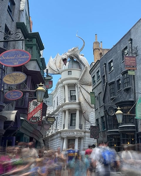 Ein großer, flügelspannender Drache sitzt auf der Kuppel der Gringotts Bank am Ende der belebten Winkelgasse in den Universal Studios.