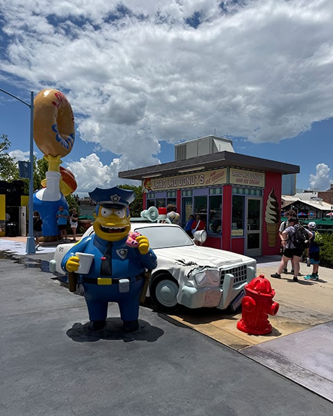 Eine große Figur von Chief Wiggum steht mit Kaffee und Donut neben seinem Polizeiauto vor dem „Lard Lad Donuts“-Kiosk in den Universal Studios Florida.