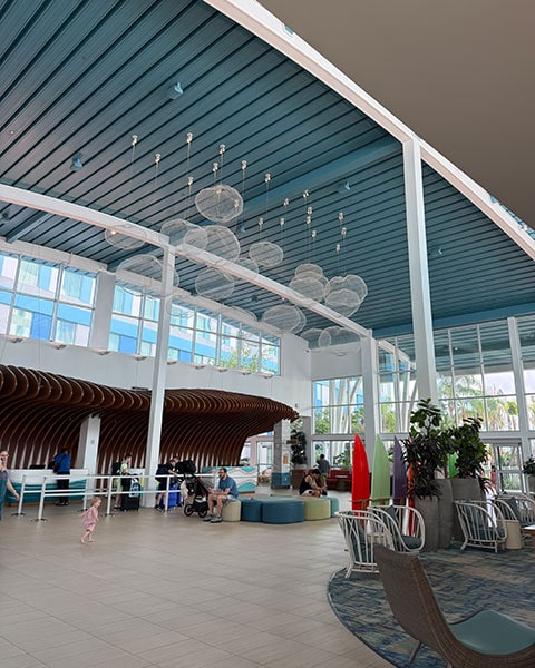 Die helle, moderne Lobby des Surfside Inn and Suites mit hohen weißen Säulen, blauer Decke, wolkenartigen Hängeleuchten und einem geschwungenen Holz-Rezeptionstresen.