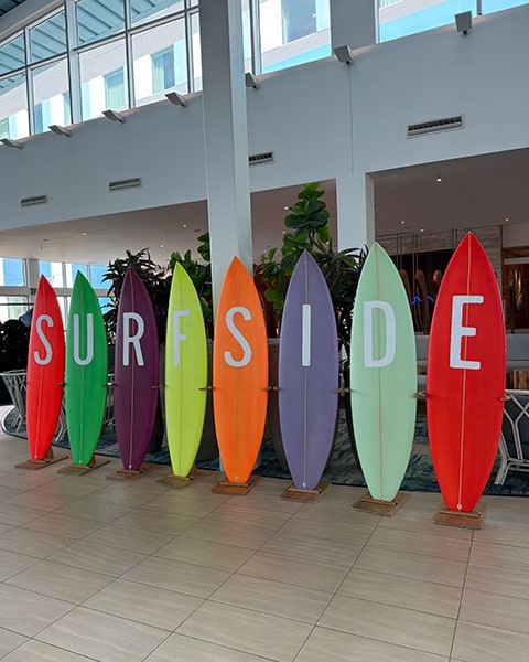 Acht bunt aufgestellte Surfbretter in einer Hotel-Lobby, die zusammen das Wort „SURFSIDE“ in großen weißen Buchstaben bilden.